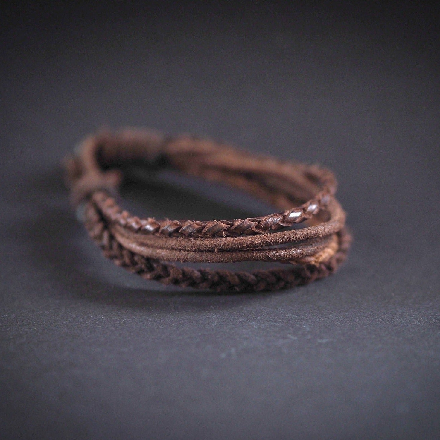 Brunt läderarmband med flätade band fotograferat på mörk bakgrund