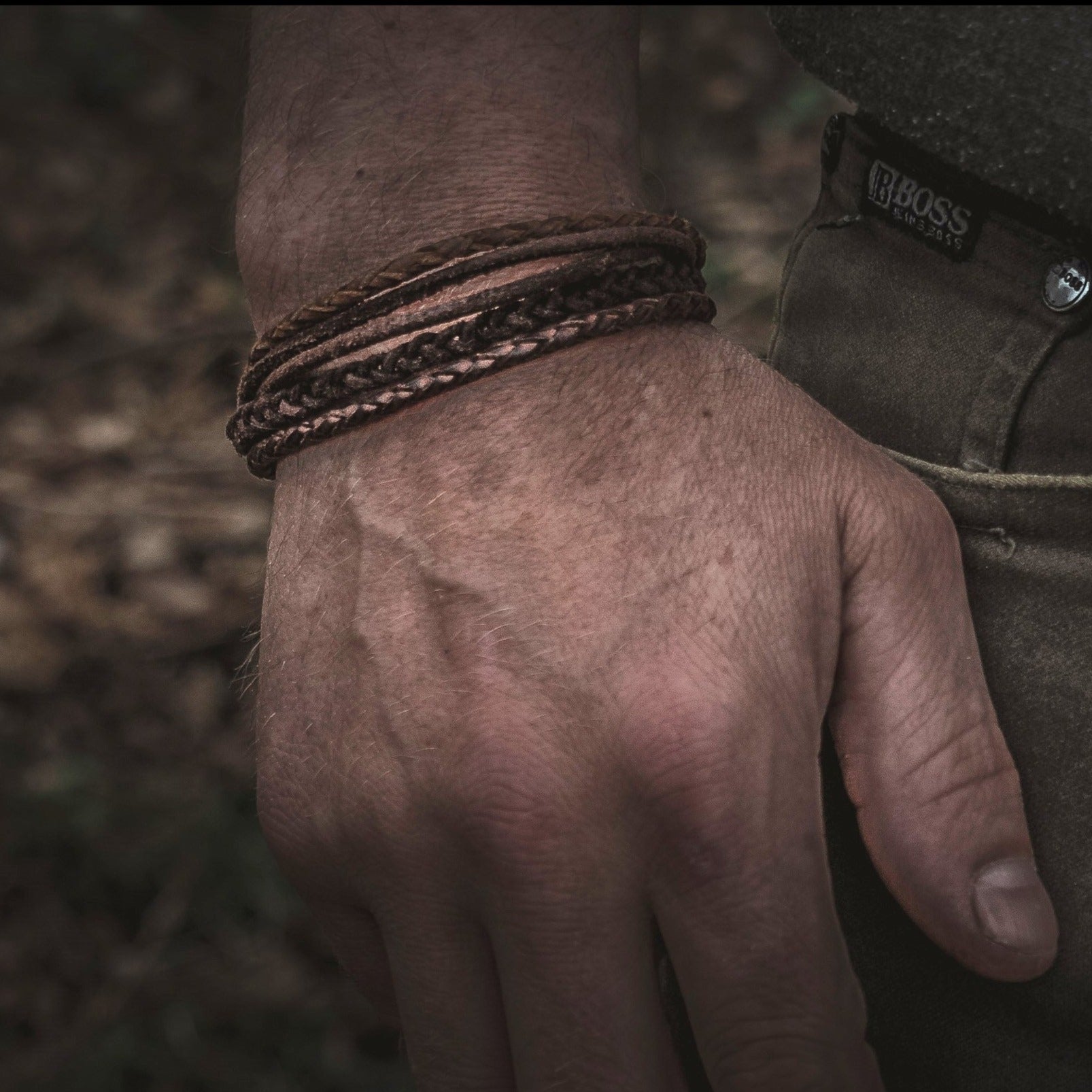 Brunt läderarmband med flätade band på en persons handled, visar hur produkten bärs