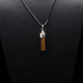 Tigeröga-hänge på mörk bakgrund med silhuett från silverfärgad mässingshållare och mörkgrå lädersnöre, professionell smyckefotografi