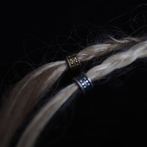 Two Skäggpärla-Tennan brass beard beads worn on braided hair strands, demonstrating styling and craftsmanship detail