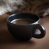 Svart eldad lerkoppar med öra i Birka-inspirerad stil. Glänsande svart yta från milbränning. Rund form med robust handtag.