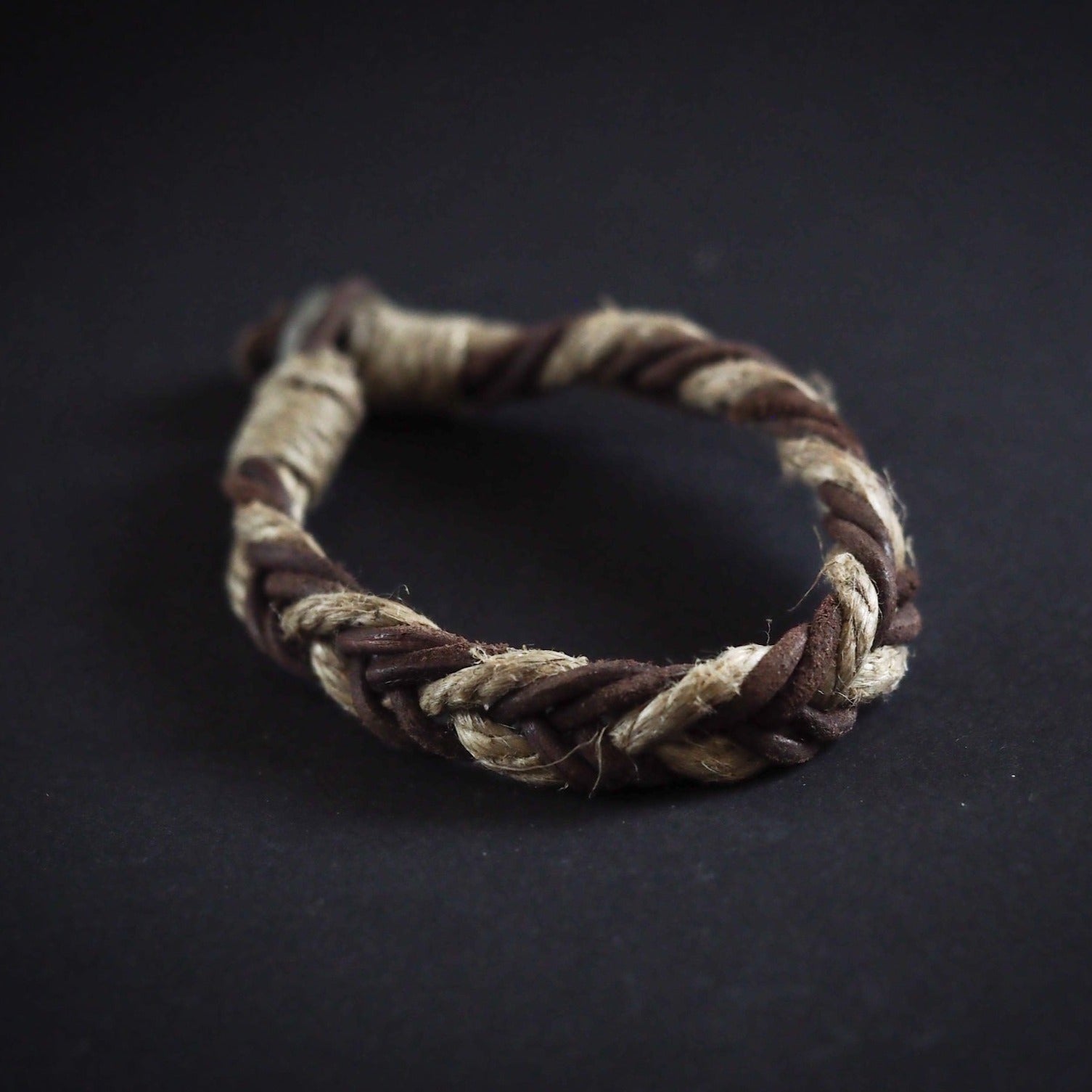 Fjalar vikingaarmband med flätad design från brunt läder, bårs på manlig handled mot naturlig bakgrund med växter.