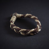 Fjalar Viking bracelet with braided design in brown leather, worn on male wrist against natural background with plants.
