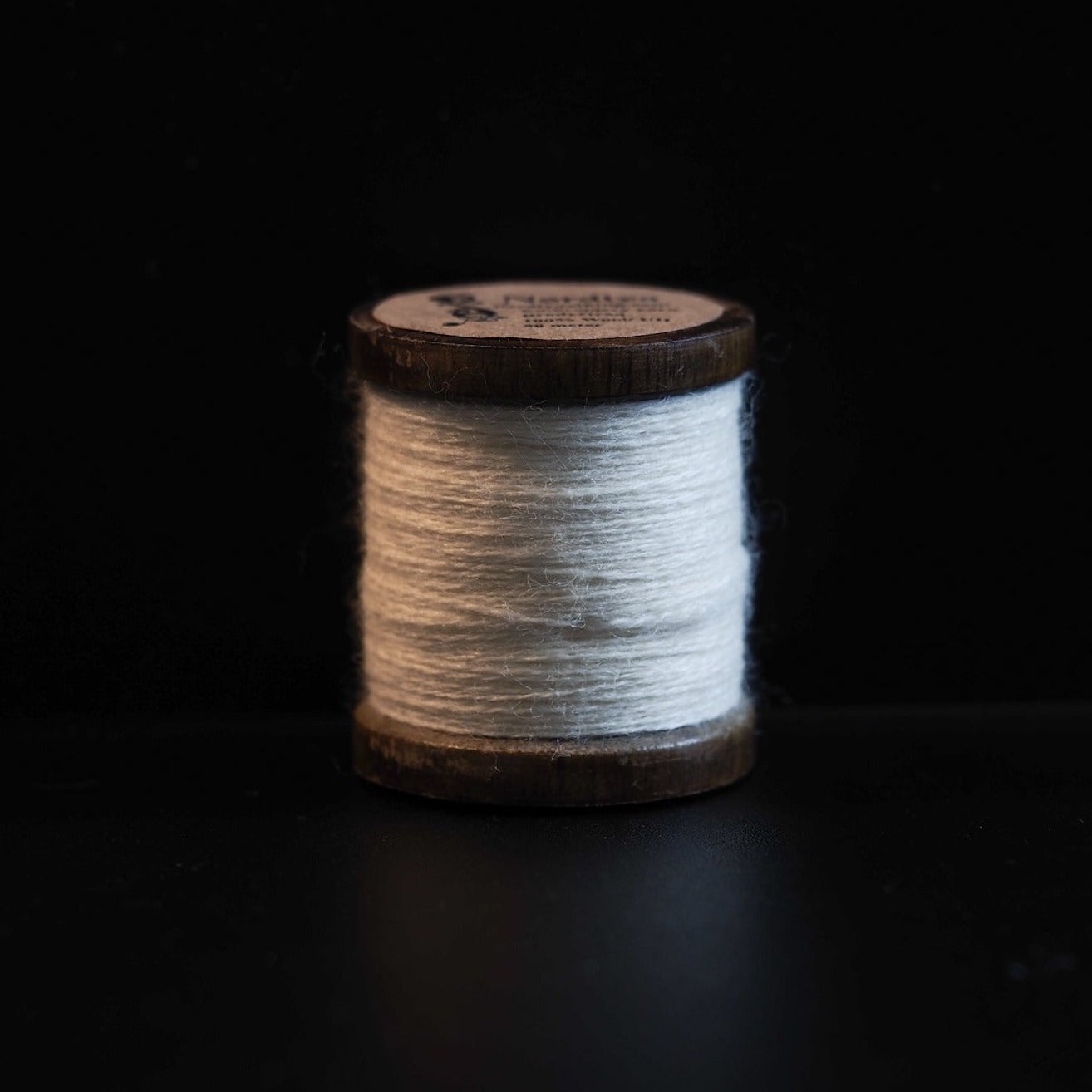 Naturvit brodyrtråd i 100% ull på träspole. Traditionell spole med mörkbetsad träram, cirka 50 meter tråd. Handarbetsmaterial för broderi och nålarbete.