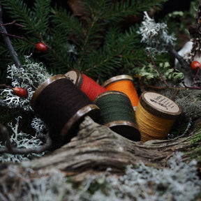 Several embroidery threads in different colors on wooden spools arranged on a tree stump in a forest setting with moss and berries
