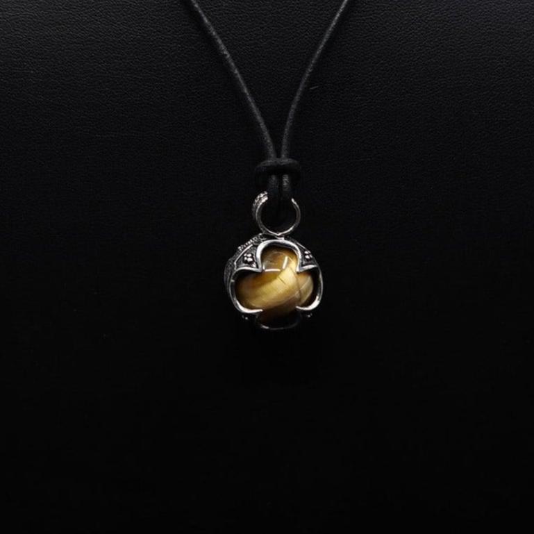 Silverpläterad gotlandshänge med tigeröga hängande på svart läderband. Tigeroögestan glänser varmt i sitt vikingiskt utsmyckade silverskal med ornamentala hörndetaljer.