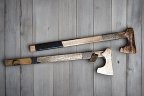 Två handsnidade träyxor med varierade träfärger och svart läderhandtag på träbakgrund