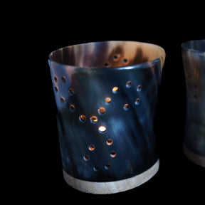 Bockhornsljuslykta med Triskele-mönstret - tre spiralformade cirkulära hål arrangerade i symmetrisk rotationsmönster. Upplysta inifran med varm orange-gul glöd synlig genom hålen.