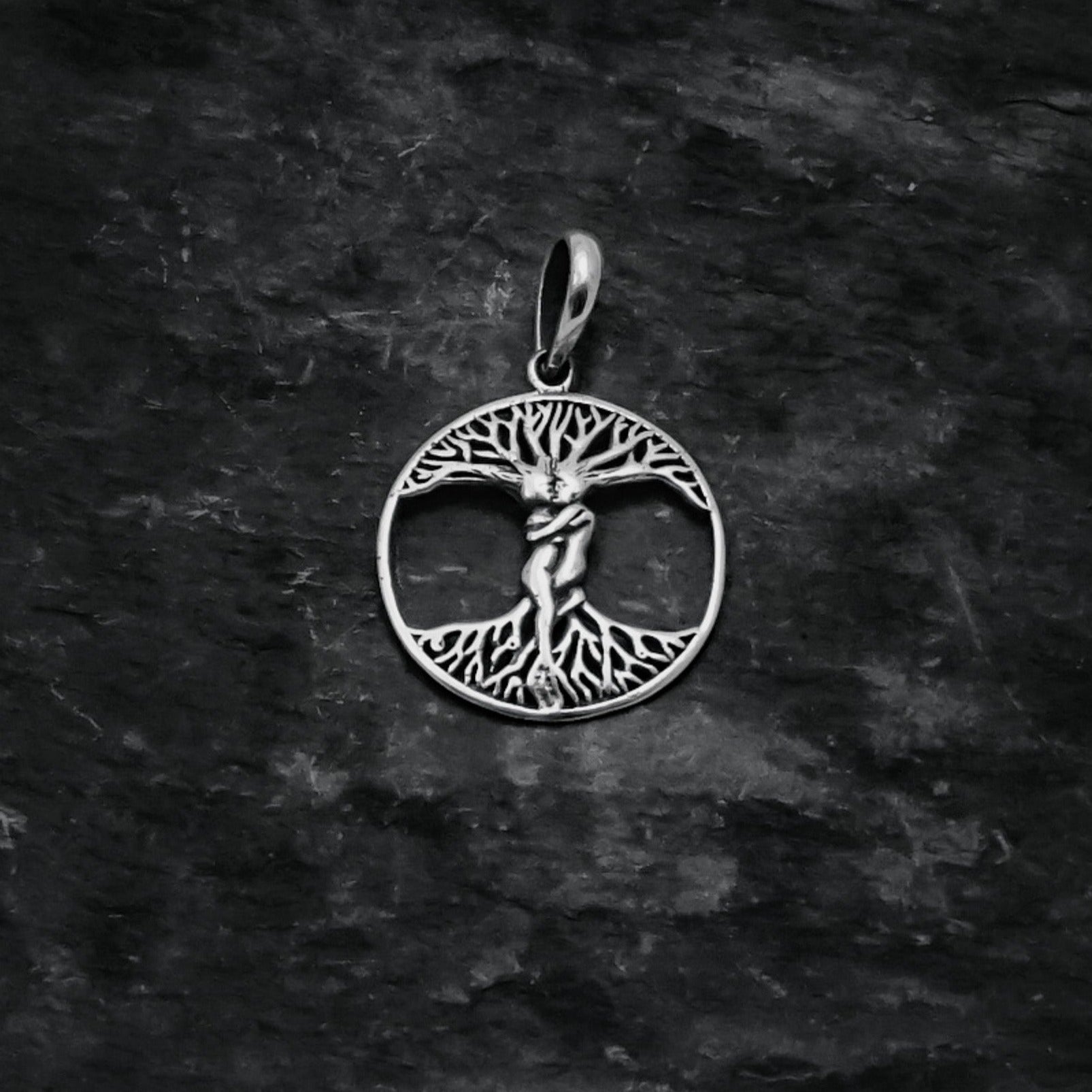 Träd-amulett fotograferad framifrån mot mörkgrå bakgrund, visar Yggdrasil-motivet med utstrålande grenar och rötter.