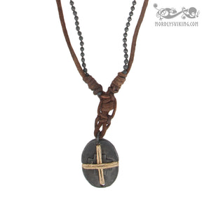 Halsband Byzans presenterad från framsidan på vit bakgrund. Visar två bruna läderband med pärlor, pilgrimskorsdesign med ovalt hänge och krusdetaljer.