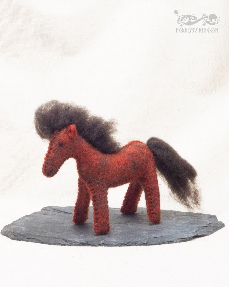 Handtovad rödbrun häst i ull med mörk man och svans, stående på skifferplatta sedd framifrån