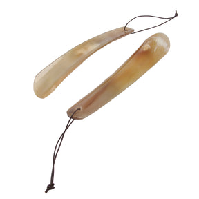 Två skohorn i naturligt horn med lädersnören, i ljust gulbrun nyans mot vit bakgrund