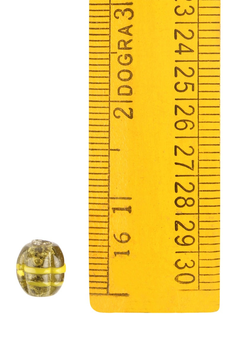 En melonpärla av glas med gul mässingsomslutning framför en gul måttstock för skalreferens, visar pärlans små dimensioner omkring 9-10mm