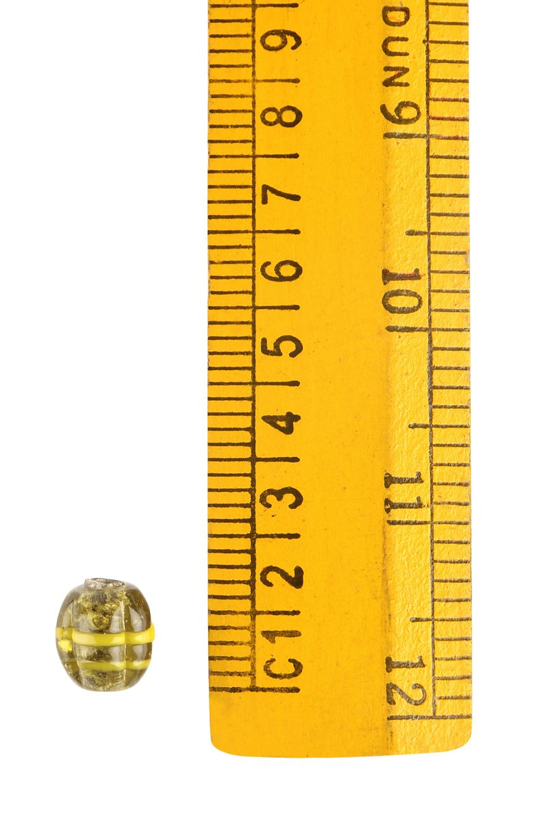 En melonpärla med gul mässingsomslutning framför en centimetermas för att visa storleken, omkring 9-10mm i diameter