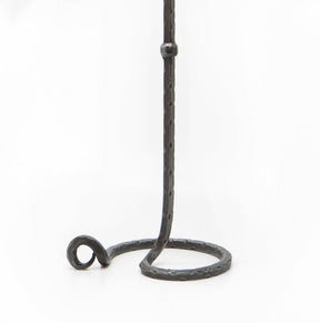 Lavatein ljusstake i hand-smiddat järn mot vit bakgrund, visar den höga släta stenen med stor cirkulär bas och dekorativ ringdetalj. Mörk galvaniserad finish med synlig smidesmärkning.