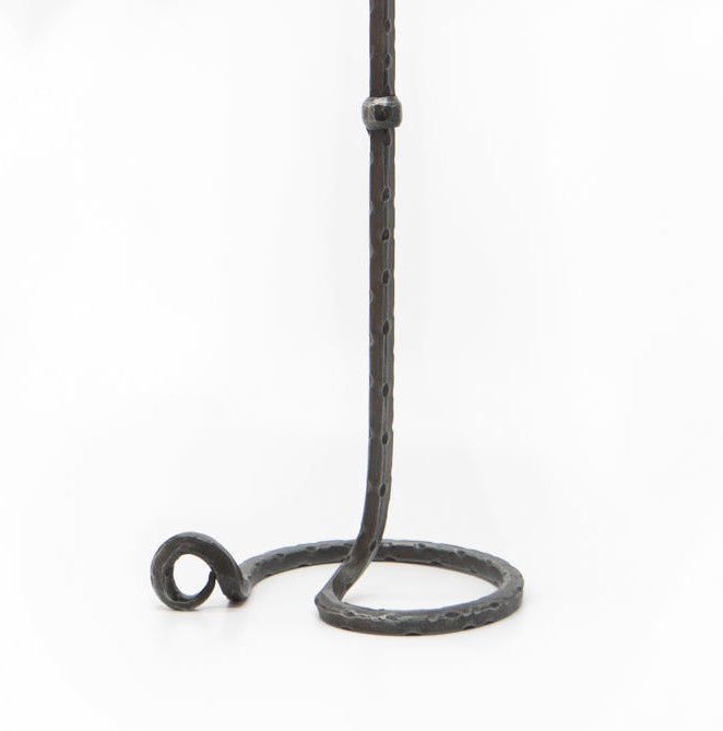 Lavatein ljusstake i hand-smiddat järn mot vit bakgrund, visar den höga släta stenen med stor cirkulär bas och dekorativ ringdetalj. Mörk galvaniserad finish med synlig smidesmärkning.