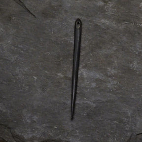 Nålbindingsnål av horn i svarttonart, fotograferad på naturlig skogsmarksbakgrund med mossa och växtliv