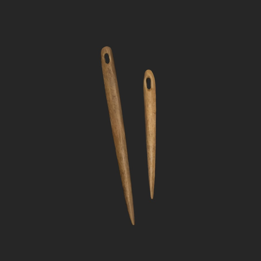 Nålbindingsnål av trä omkring 7 cm långt, fotograferad på skogsmarksbakgrund med mossa och naturlig miljö