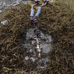 Vargkors halsband på naturlig stenyta med mossa, brunt läder med pärlad dekoration, metallkors och varghovedе vänd nedåt
