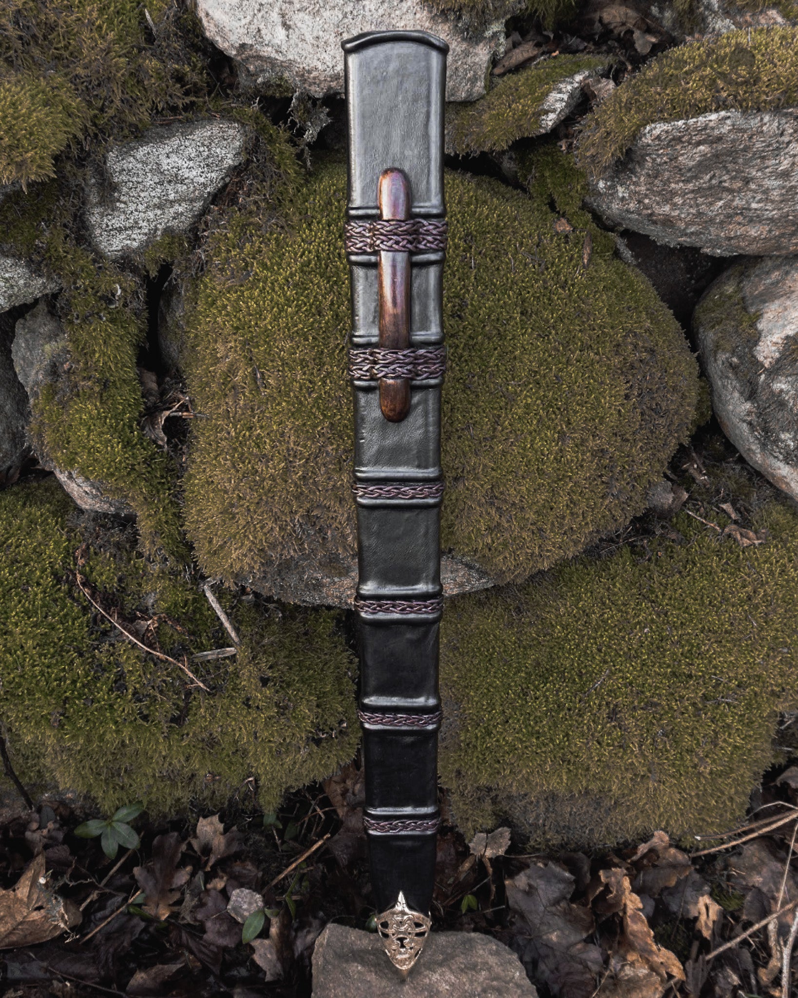 Svärdskida, Braid of glory - läderslida med flätad metalldekor och trähandtag, vertikalt perspektiv på stenar