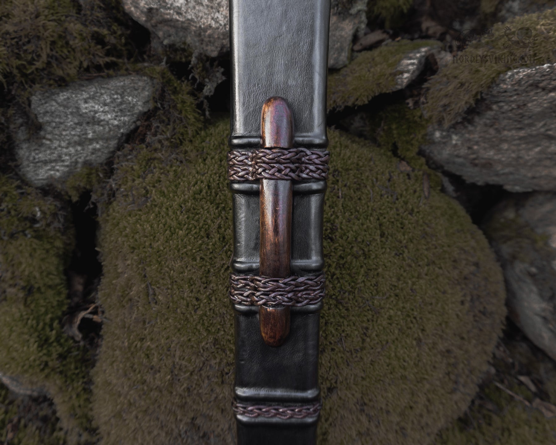 Svärdskida detalj - närbild på läderslida med flätade metallband och trähandtag, vikingatida design