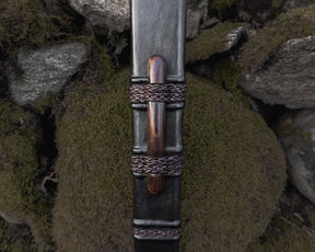Svärdskida detalj - närbild på läderslida med flätade metallband och trähandtag, vikingatida design