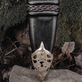 Svärdskida med flätad dekor - läderslida för svärd med vikingtida sköldsymbol vid spetsen, fotograferad mot mossiga stenar