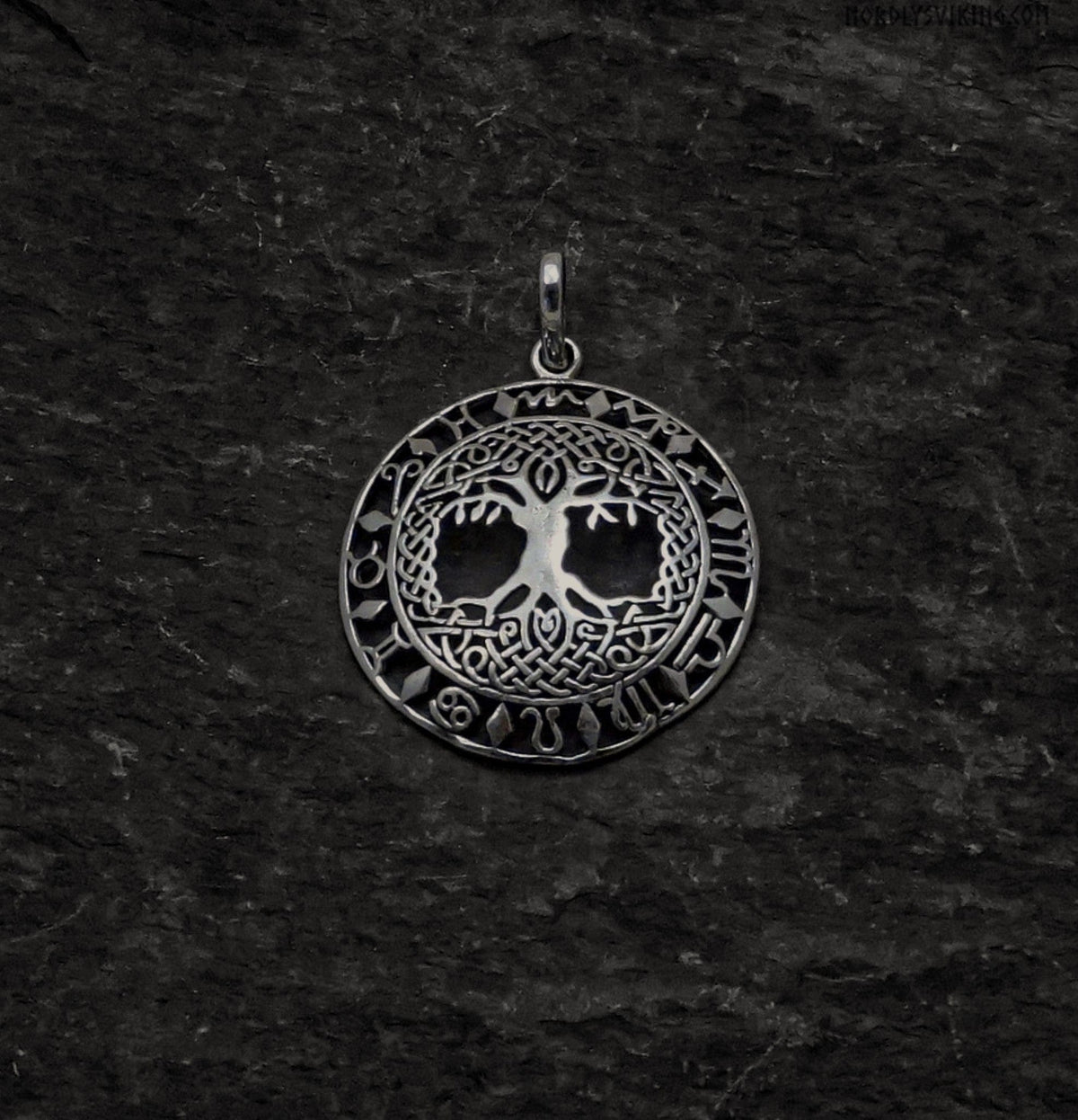 En silverpläterad Yggdrasil hänge med zodiakala symboler arrangerade i en cirkel runt träd motiv. Visar detaljerad mässingsarbete på mörk bakgrund.